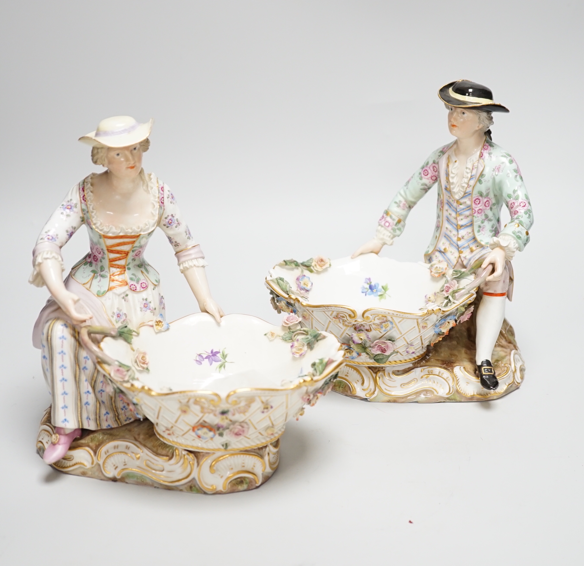 A large pair of Meissen salts in the form of a seated man and a woman in 18th century dress (a.f.), 21cm high